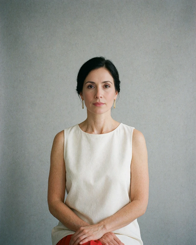 Portrait of a woman with a smooth low updo and gold earrings seated against a fog gray backdrop