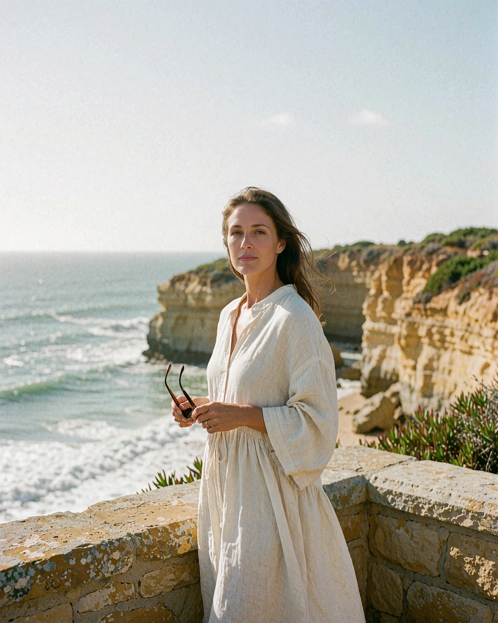 Woman in a cream linen dress standing on a cliff-top terrace above the Pacific Ocean near La Jolla