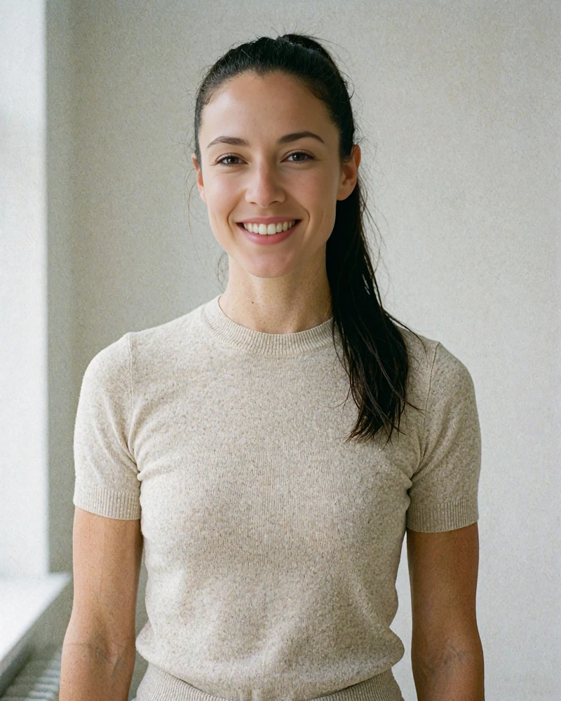 Portrait of an athletic woman with a high dark ponytail wearing a fitted oatmeal knit top in a bright room