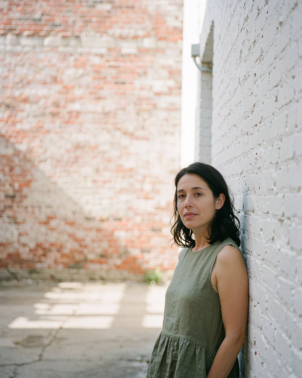 Woman in an olive linen dress standing beside a whitewashed stucco wall in the Pearl District of San Antonio